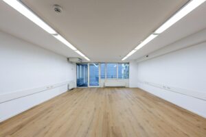 Leeg, wit kantoorpand met houten vloer en grote ramen aan de Prins Hendrikkade.